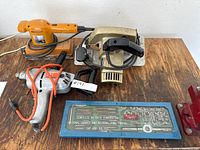 Photo of three electric hand tools on a wooden surface with a blue metal tap and die set box, showing the full lot content.