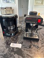 Two coffee machines including NutriChef espresso/cappuccino maker and standard drip coffee maker side by side on counter.