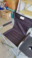 Folding black camping chair with padded armrests and attached side table with two cup holders, displayed in warehouse setting.