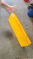 Yellow plastic table folded for compact storage with integrated handle visible