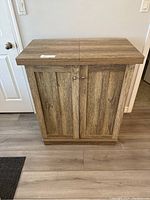 Closed wooden liquor cabinet with two doors, compact size, medium wood grain finish