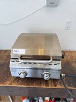 Front view of Megamaster portable grill showing two control knobs and gas hose on wooden surface.