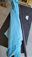 Folded light blue patio umbrella with visible fabric and part of steel pole lying on a surface.