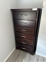 Solid wood highboy dresser positioned against wall, six drawers closed, dark brown finish with metal handles visible.