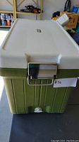 Front close-up view of vintage green Coleman cooler with white lid, showing metal latch and drainage spigot.