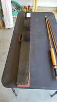 Fishing rod and long carrying case placed on a dark table viewed from the side showing length and handle type.