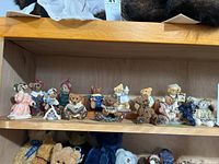 Shelf with a row of bear figurines, each dressed in various clothing styles including dresses and suits; hand-painted and detailed.