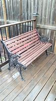 Wooden slat bench with ornate cast iron frame shown on wooden deck near fence.