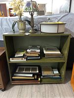 Front angle of wooden shelf unit showing two compartments filled with picture frames (contents not included). Olive green finish.