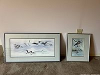 Two framed Sue Coleman prints displayed on carpet against a wall, one large horizontal and one smaller vertical, both feature birds and nature themes.