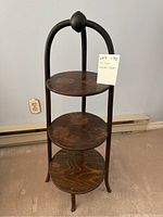 Full view of the 3 tier wooden round shelf with curved supports and rounded finial top.