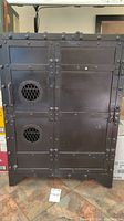 Front view of black metal cabinet showing rivet accents and door with vented circular windows.