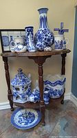 Wide view of assortment of blue and white porcelain items on wooden three-tier table showing vases, mugs, figurines, and decorative pieces.