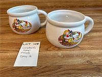 Two white ceramic mugs with round bodies and handles featuring vintage Campbell's design of children in a kitchen.