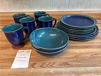 Full view of all dishware items grouped on a wooden counter showing mugs, bowls, dinner plates, and salad plates.