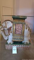 Side view of ornate porcelain elephant base with round glass tabletop resting on it, showing detailed decorations and patterns.