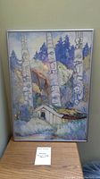 Framed watercolour print with visible Haida totem poles and nature background, shown on a wooden surface with a small note visible.