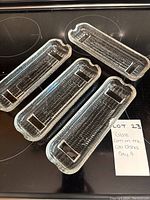 Four clear glass corn on the cob dishes arranged in a group showing textured corn design and handles on each end.