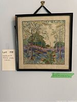Full view of needlepoint forest artwork in black frame hanging on wall with dimensions label.