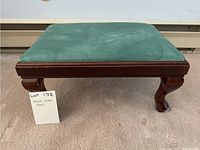Front view of small foot stool showing green vinyl cushioned top and wooden frame with carved legs.