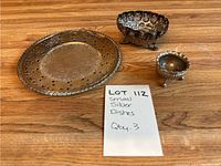 Photo of all three small silver dishes together showing the plate and two footed dishes with their detailed designs and tarnished finish