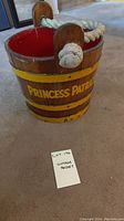 Full view of the vintage wooden bucket with 'Princess Patricia' lettering and rope handles on carpeted floor.