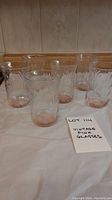 Set of six vintage pink glasses with etched floral patterns on a white surface.