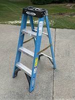 Full view of the blue Werner 4 foot step ladder with aluminum steps and top black plastic tool tray, set up on concrete outdoors.