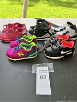 Lot of five pairs of baby shoes on a black surface outdoors showing various colors and designs.