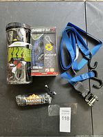 Photo showing all items in the lot including a container of black bungee cords with hooks, boxed Bungee-O Net 7 count, blue ratchet tie-down strap, and a bundle of paracord.
