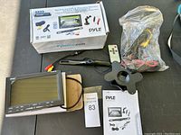 Full kit items placed on table including LCD monitor, backup camera, remote, manuals, and wiring harnesses.