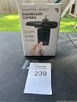 Front view of the boxed Sharper Image dashboard camera showing camera image and key features: wide angle lens, flip down and rotate for 360° views, clear views day or night.