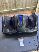 Front view of black electric foot massager showing fabric foot sleeves and central control panel.