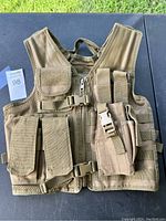 Front view of brown tactical vest on outdoor surface, showing zipper, buckle, flap and vertical pouches