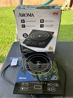 Boxed Aroma Extra Large induction cooktop outside showing product and features on box, cooktop placed in front.