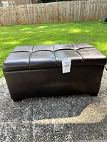 Front view of the rectangular dark brown leather storage chest with a padded top, showing eight tufted squares on the lid.