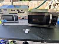 Hamilton Beach microwave oven with original box placed on a table under daylight.