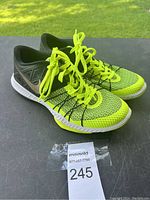Side angled view of neon yellow and black Nike running shoes on a dark surface with greenery background.