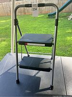 Full view of the foldable two-step stool ladder with metal frame and two black plastic steps outdoors on a table.