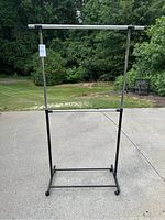 Full view of the two-tier garment rack standing on outdoor concrete surface, showing structure and wheels.