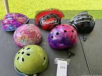 Overview of 6 youth bike helmets together on a table, showing variety of colors and styles