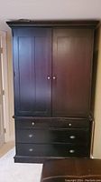 Front view of the black Vermont Tubbs armoire showing two doors and three drawers with round handles.