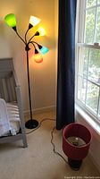 Adjustable floor lamp turned on showing five different colored cone lampshades: green, black, yellow, blue, and red.