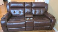 Front view of brown electric reclining loveseat showing tufted seats, center console with cup holders and nailhead trim