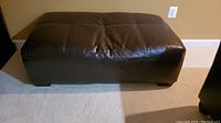 Front and side view of dark brown oversized ottoman with visible peeling damage on upholstery.