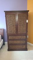 Front view showing the two cabinet doors with woven wicker panels and three drawers below, also with wicker panels and round metal knobs.