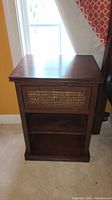 Full front view of the dark wood nightstand showing wicker drawer front and open shelf below.