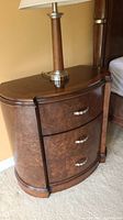 Side view of Pulaski nightstand with lamp on top, showing the curved curved front and burl wood finish.