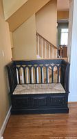 Black wooden storage bench with a natural wicker seat cushion and three front drawers shown in partial side angle and full front views, highlighting the gothic arch cutout pattern and missing drawer pull on one drawer.