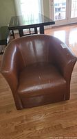 Front view of brown leather swivel armchair showing cracks and wear on seat and arms